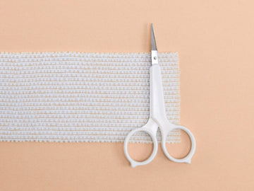 Pair of scissors and a strip of gauze on a beige background for the Plastic Surgery & Treatment section