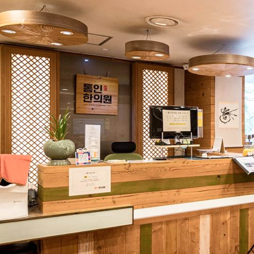 Wooden reception desk of Tong-in Clinic with a computer monitor and various items in a room with wooden decor. 